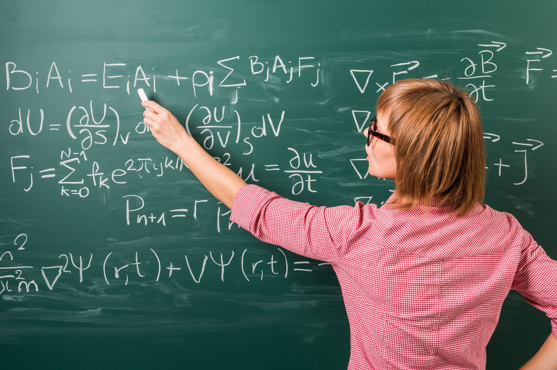 Female teacher standing against chalkboard, explains, solves physics